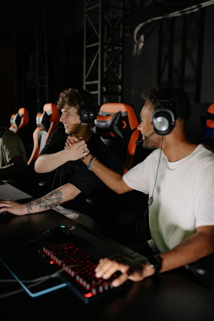 Two excited gamers shake hands, celebrating a win on their gaming setup indoors.